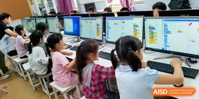 Three young students work together at a computer station in a bright lab focusing on a coding project shown on the screen at the Beijing Haidian Rising Experimental School