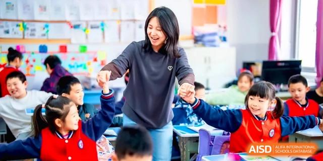 A joyful teacher laughs while holding hands with her students during a fun interactive group activity in a classroom at the Beijing Haidian Rising Experimental School