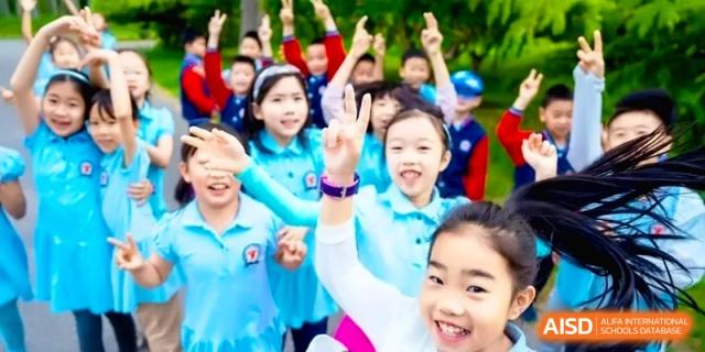 A group of excited elementary students in blue uniforms wave and smile brightly for a group photo outdoors at the Beijing Haidian Rising Experimental School