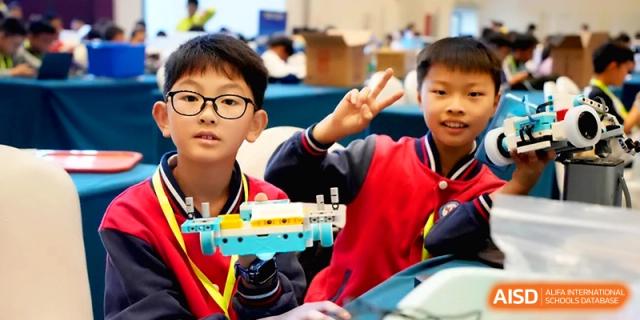 Two boys in school uniforms smile while holding up a robotic vehicle they built during a science and technology workshop at the Beijing Haidian Rising Experimental School