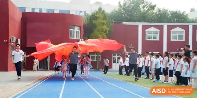 Students and staff carry a massive red flag across a blue running track during a spirited school sports day at the Beijing Haidian Rising Experimental School