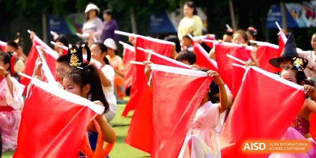 A row of students hold up large red rectangular banners in a synchronized display during an outdoor school performance at Beijing Haidian Rising Experimental School