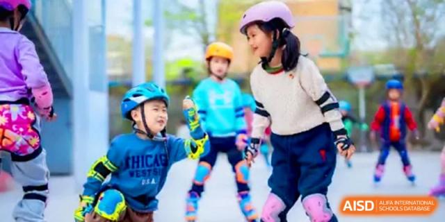 Two young students wearing helmets and safety gear practice inline skating together on a bright day at the Beijing Haidian Rising Experimental School
