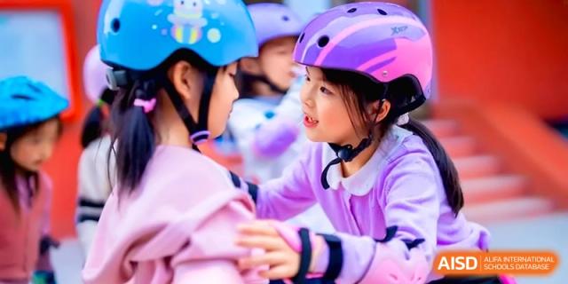 Two young girls wearing colorful helmets and skating gear smile and interact during an outdoor activity at the Beijing Haidian Rising Experimental School