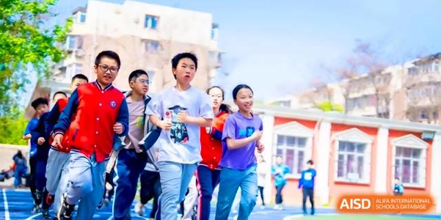 A group of students in casual athletic wear run together during a physical education class or track meet at the Beijing Haidian Rising Experimental School