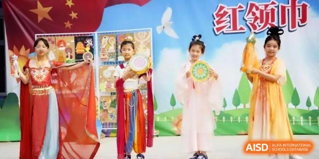 Two students dressed in traditional Chinese attire stand on a stage in front of a colorful backdrop at the Beijing Haidian Rising Experimental School