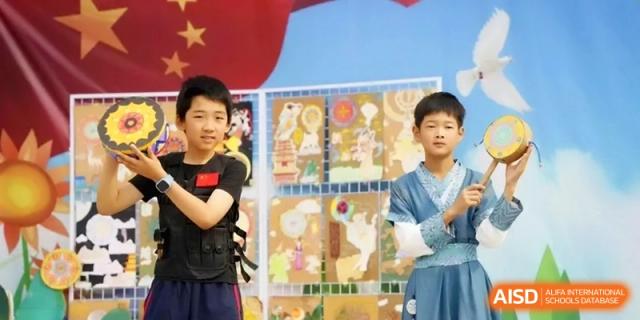 Two boys stand in front of a display of student artwork during a school exhibition or cultural festival at the Beijing Haidian Rising Experimental School