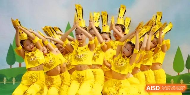 A large group of students in bright yellow traditional costumes perform a synchronized dance on stage at the Beijing Haidian Rising Experimental School