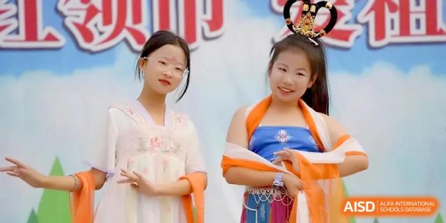 Two girls dressed in elegant traditional silk clothing pose together for a photo during a cultural event at the Beijing Haidian Rising Experimental School