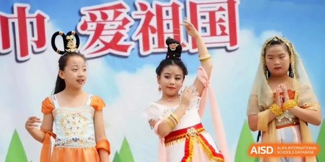 A young girl in a white and red traditional dance costume performs a graceful routine on stage at the Beijing Haidian Rising Experimental School