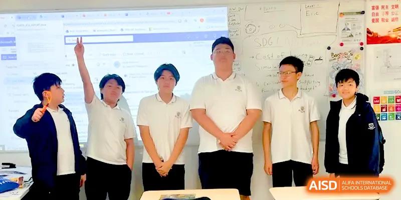 Four male students in white polo shirts standing at the front of a classroom during a presentation at HD Beijing School.