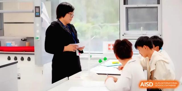 A teacher in a black blazer holding documents and speaking with a student in a classroom at HD Beijing School.