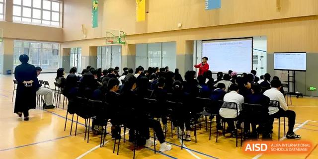 A large assembly of students in dark uniforms sitting in the gymnasium watching a presentation at HD Beijing School.