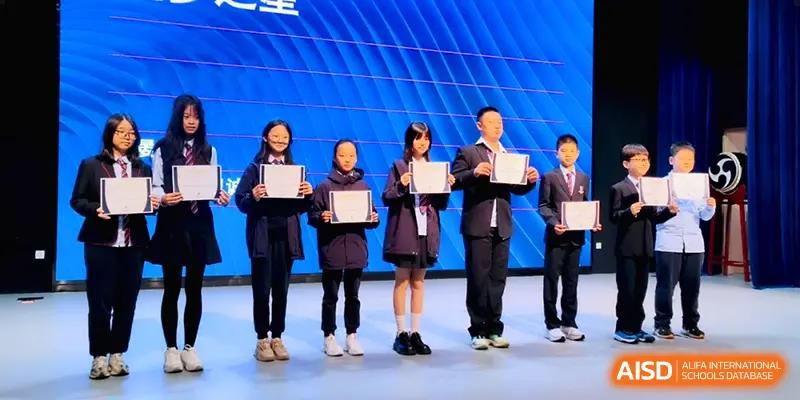 Five students standing on a stage holding white certificates during an awards ceremony at HD Beijing School.