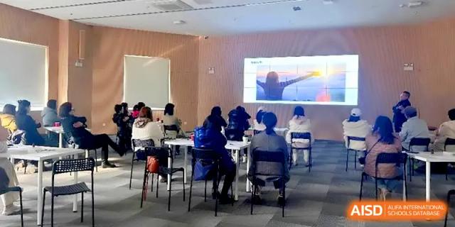 An audience of students and staff watching an inspirational video on a large screen in a meeting hall at HD Beijing School.