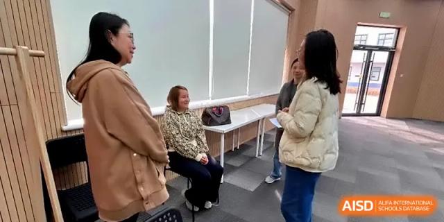 Three women engaged in a friendly conversation in a brightly lit indoor school office or meeting room at HD Beijing School.