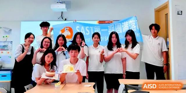 A group of students in white shirts gathered together for a celebratory photo with a cake at HD Beijing School.