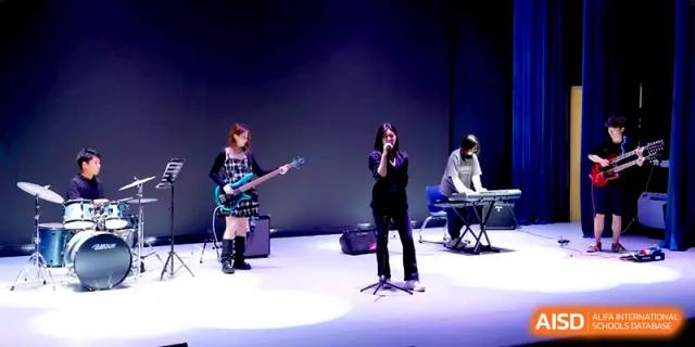 A student band performing on stage with a guitarist and vocalist under professional stage lighting at HD Beijing School.