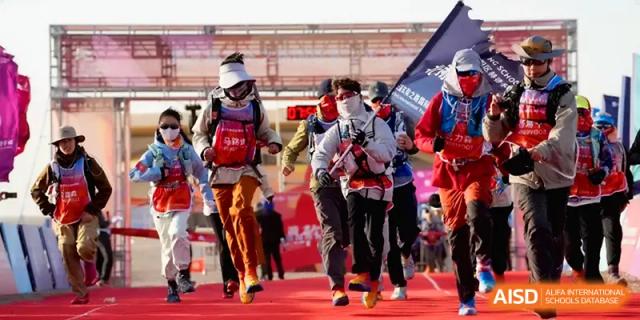 A group of student hikers in full gear and face masks walking on a red track during a sports event at HD Beijing School.