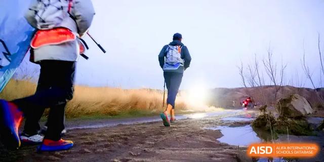 A student hiker seen from behind walking toward a bright sun on a rugged outdoor path at HD Beijing School.