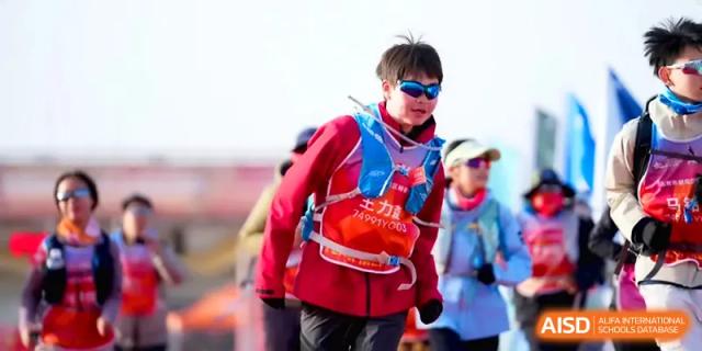 A student hiker wearing a red jacket and safety vest walking through a desert landscape during a trek at HD Beijing School.
