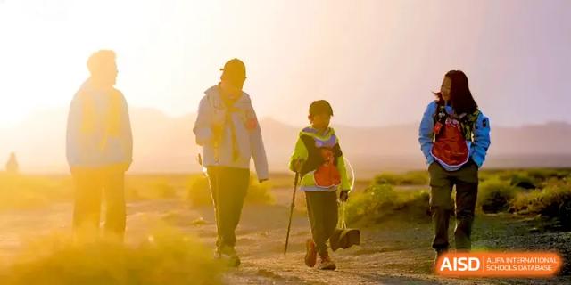 Two students walking through a dusty, sunlit landscape during a challenging outdoor hiking trip at HD Beijing School.
