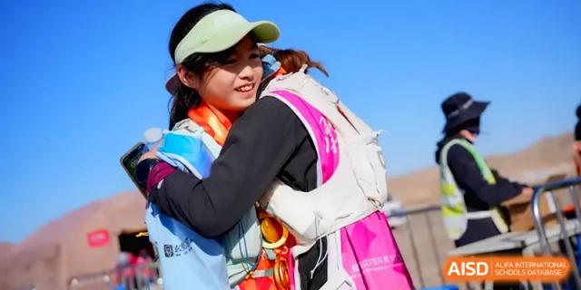 Two female students sharing a warm hug while wearing their hiking gear and safety vests at HD Beijing School.