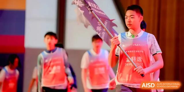 A student in a pink safety vest carries a purple flag while marching with peers during an outdoor school activity at HD Beijing School.