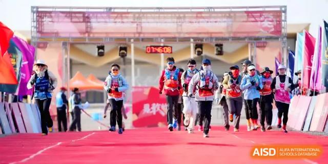A group of students in red and blue athletic gear sprints toward the finish line on a red carpet during a race at HD Beijing School.