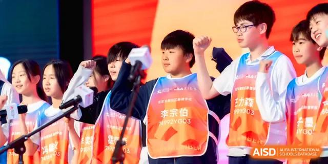 A young student in an orange safety vest raises a fist in a gesture of determination during a school event at HD Beijing School.