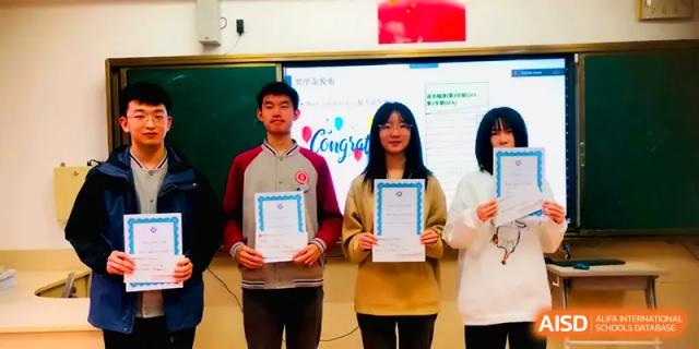 Three students stand proudly at the front of a classroom holding award certificates at Qingdao Experimental High School.