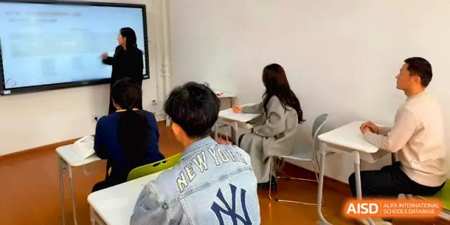 Students sit at their desks in a bright classroom while listening to a teacher's lecture at Qingdao Experimental High School.