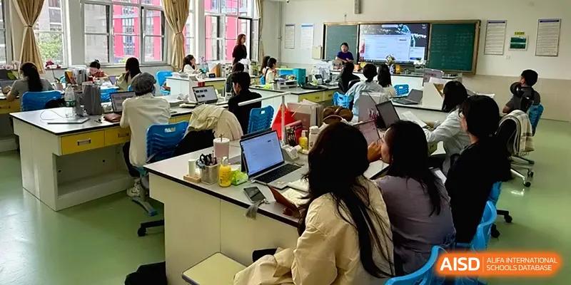 A classroom view shows students working on laptops at white laboratory-style tables at Qingdao Experimental High School.