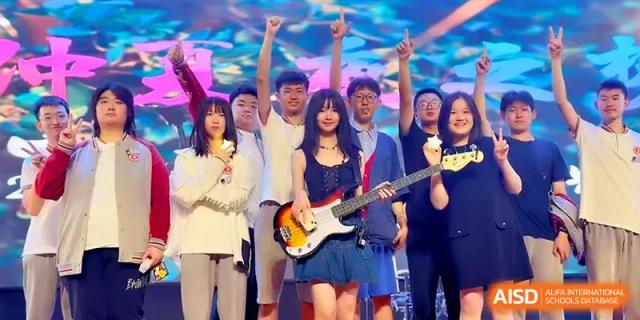 A group of students cheers enthusiastically behind a girl holding a bass guitar on a stage at Qingdao Experimental High School.