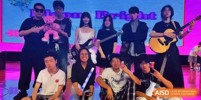 A group of students posing together for a photo, some holding musical instruments like a guitar, at Qingdao Experimental High School.