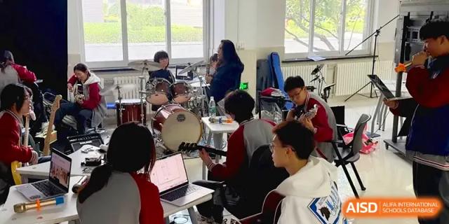 A teacher leads a group of students during a music rehearsal with drums and laptops at Qingdao Experimental High School.