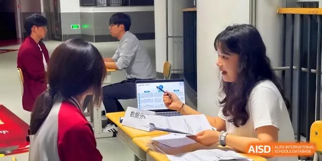 An educator points at a laptop screen while discussing paperwork with a colleague at Qingdao Experimental High School.