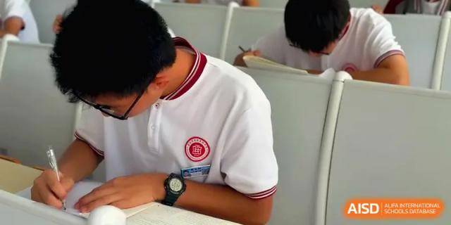 A student in a white uniform with a black watch writes in their notebook at Qingdao Experimental High School.