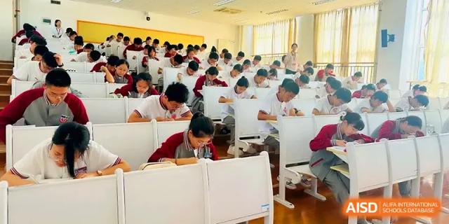 A large group of students work at desks in a spacious, well-lit examination hall at Qingdao Experimental High School.
