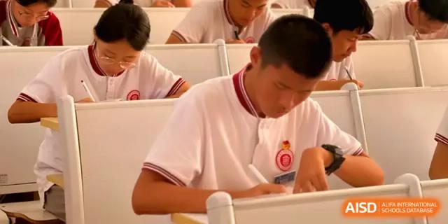 A male student leans over his desk to write carefully during an academic session at Qingdao Experimental High School.