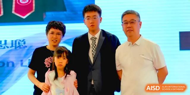 A young man in a suit and tie poses with family during a formal ceremony at Qingdao Experimental High School.