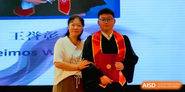 A student in a red and black graduation gown poses with a proud family member at Qingdao Experimental High School.