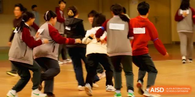 Students in tracksuits participate in a group coordination exercise on the field at Qingdao Experimental High School.