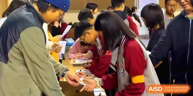 A group of students in school jackets gather around a table for a social activity at Qingdao Experimental High School.
