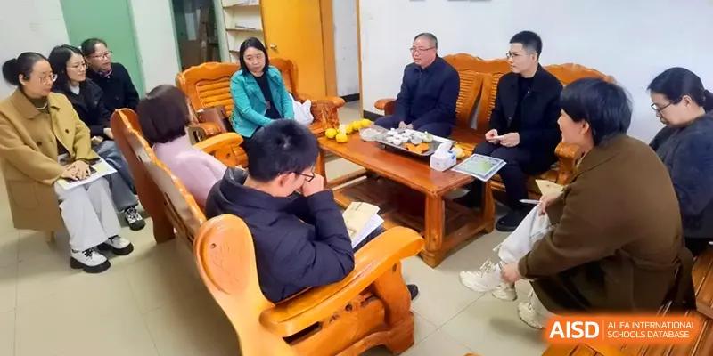 A group of adults in professional attire sit on wooden sofas in an office, engaged in a formal meeting with tea and fruit on the table at Quanzhou No. 5 Middle School.
