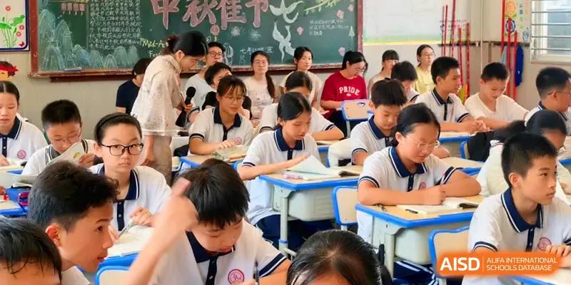Students in white and blue uniforms sit at their desks in a bright classroom, listening intently during a lecture or presentation at Quanzhou No. 5 Middle School.