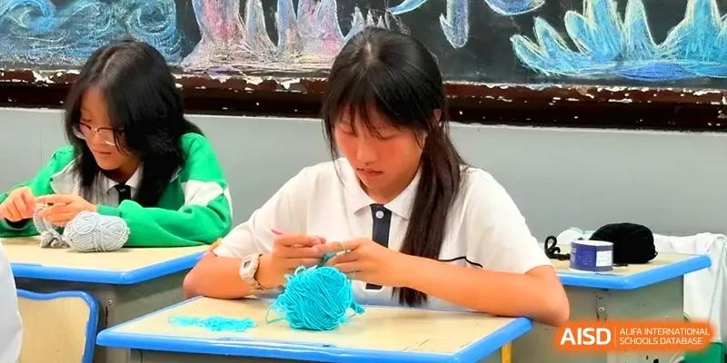 A female student focuses on a handicraft project at her desk, working carefully with bright blue yarn during an extracurricular activity at Quanzhou No. 5 Middle School.