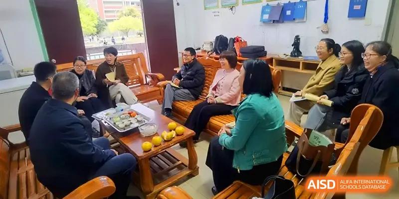 Teachers and staff gather for a collaborative discussion in a lounge area, seated on traditional wooden furniture with snacks prepared at Quanzhou No. 5 Middle School.