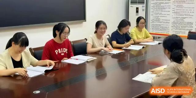 Four staff members sit at a dark wood conference table, taking notes and discussing curriculum or school administrative matters at Quanzhou No. 5 Middle School.