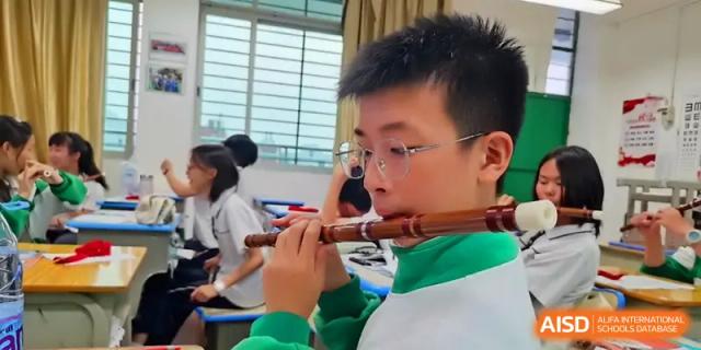 A male student in a green and white jacket plays a traditional wooden flute, practicing his musical skills during a dedicated arts period at Quanzhou No. 5 Middle School.
